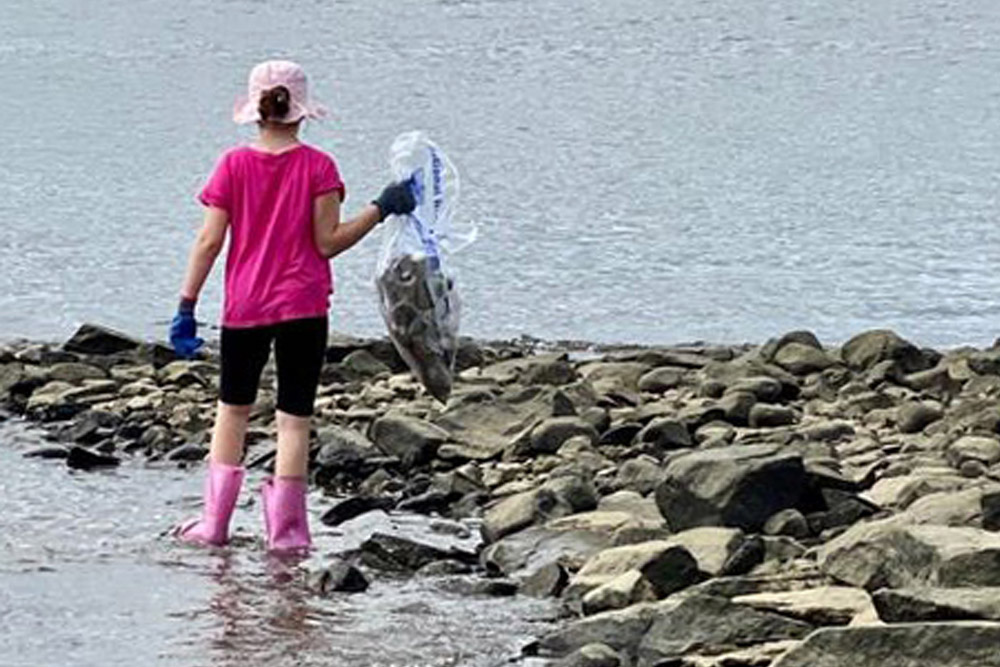 Young girl picking up trash along the shore